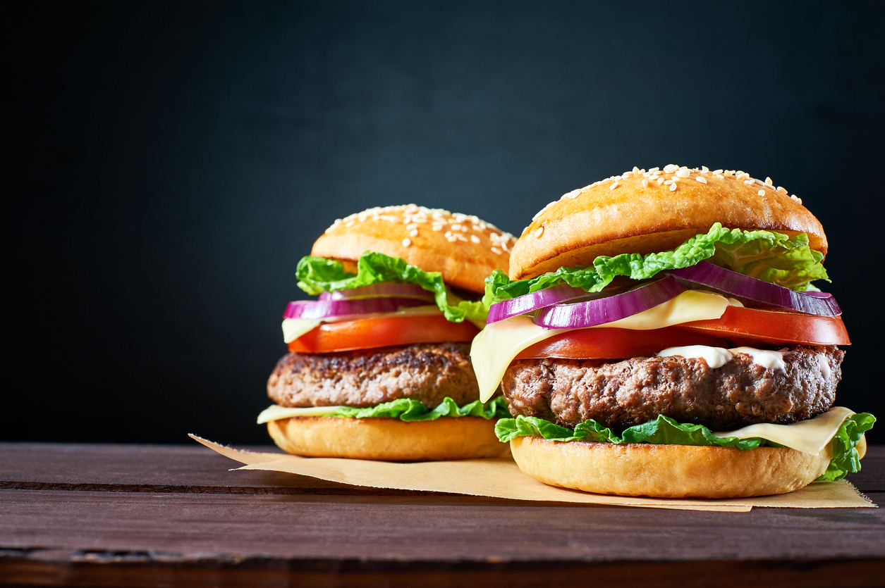 Zwei Hamburger mit Salat, Tomaten, Zwiebeln, Käse und Barbecue-Sauce, auf einem Holzbrett servier