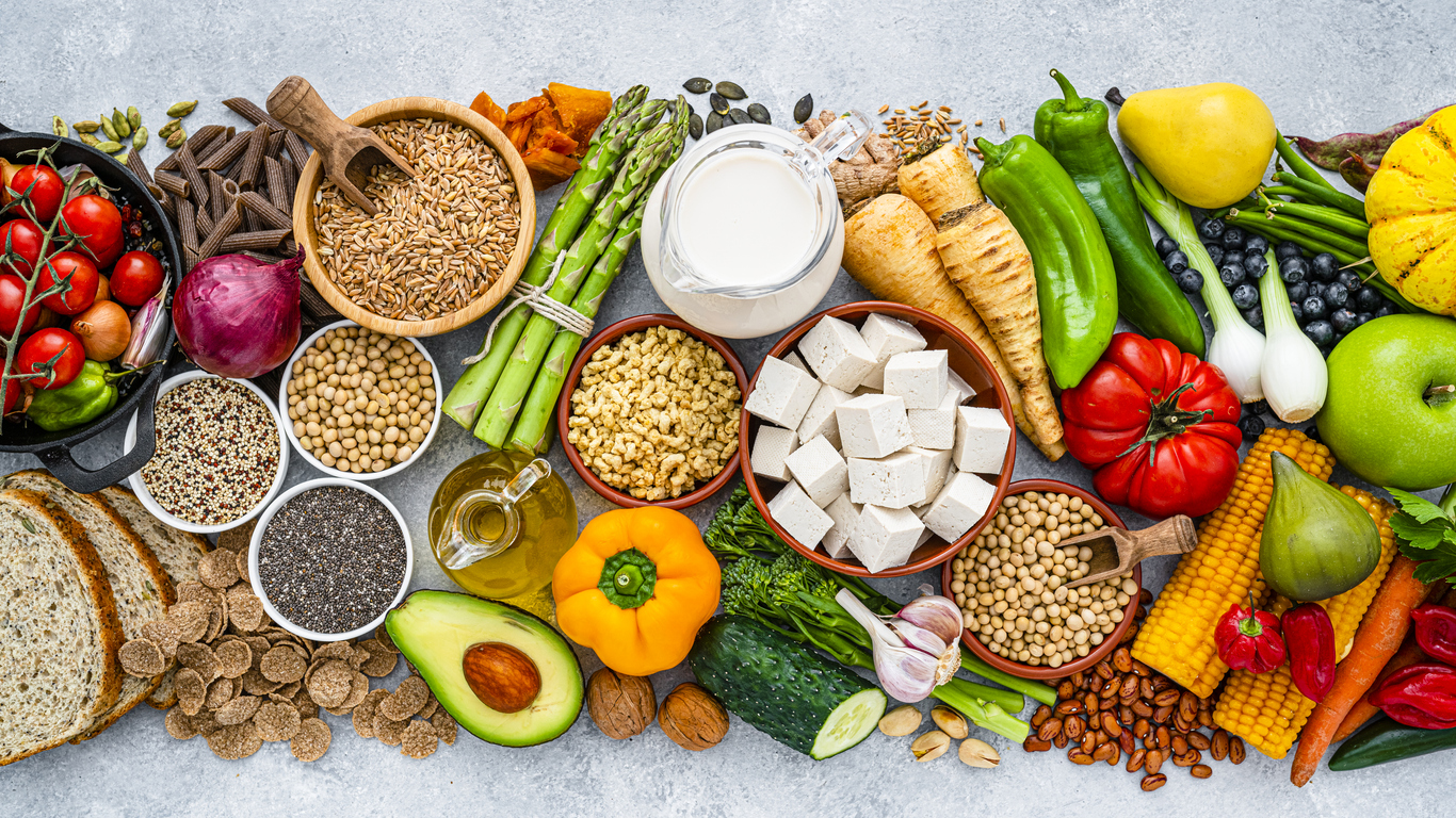 Verschiedene vegane Lebensmittel wie Gemüse, Getreide, Tofu, Nüsse und Samen