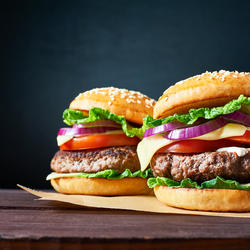 Zwei Hamburger mit Salat, Tomaten, Zwiebeln, Käse und Barbecue-Sauce, auf einem Holzbrett servier