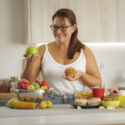 Frau hält einen Apfel und einen Muffin in einer Küche.