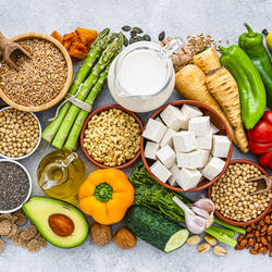 Verschiedene vegane Lebensmittel wie Gemüse, Getreide, Tofu, Nüsse und Samen